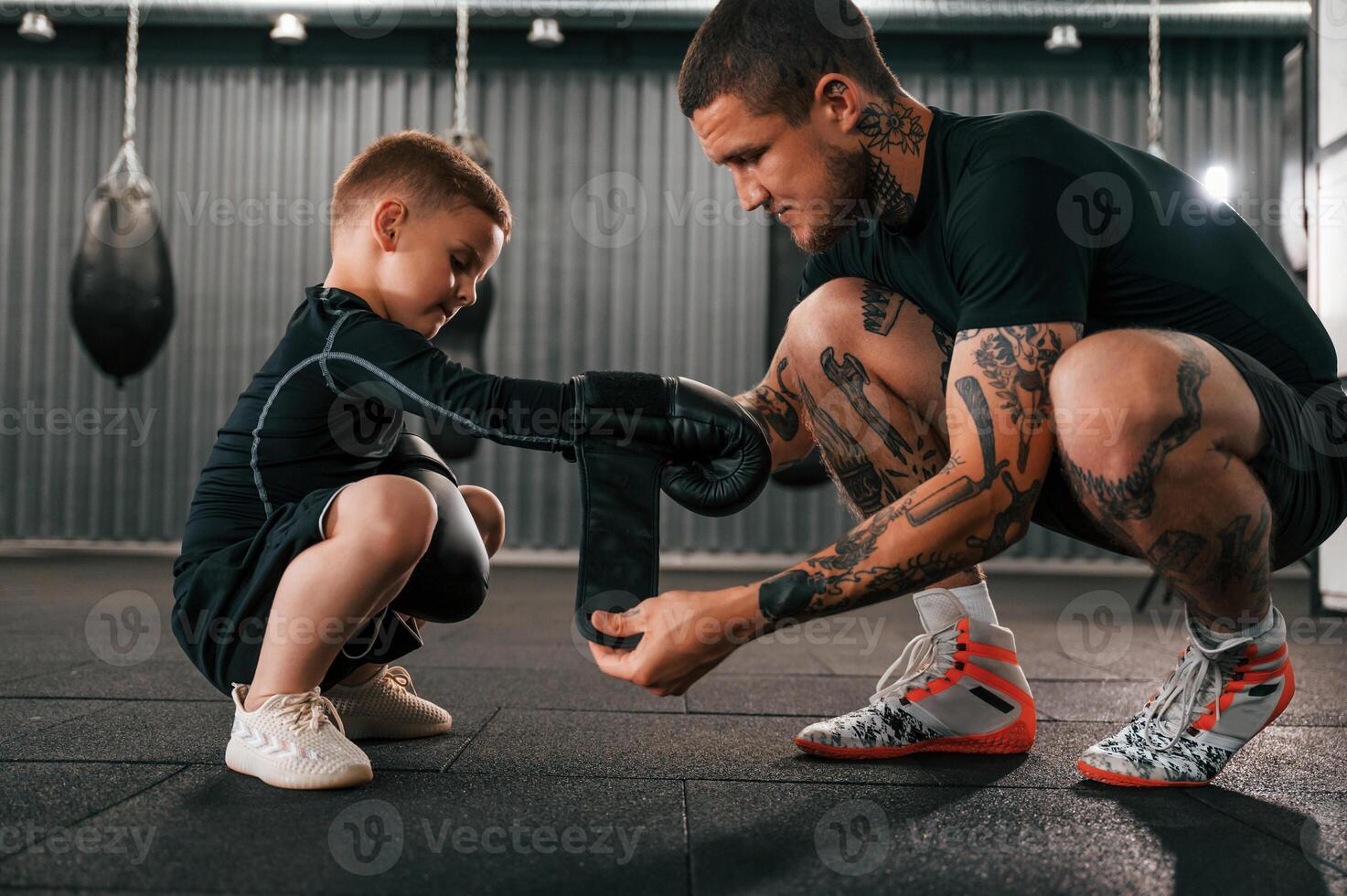 Man is helping child to wear the glowes., Coach is teaching the boy box techniques indoors photo