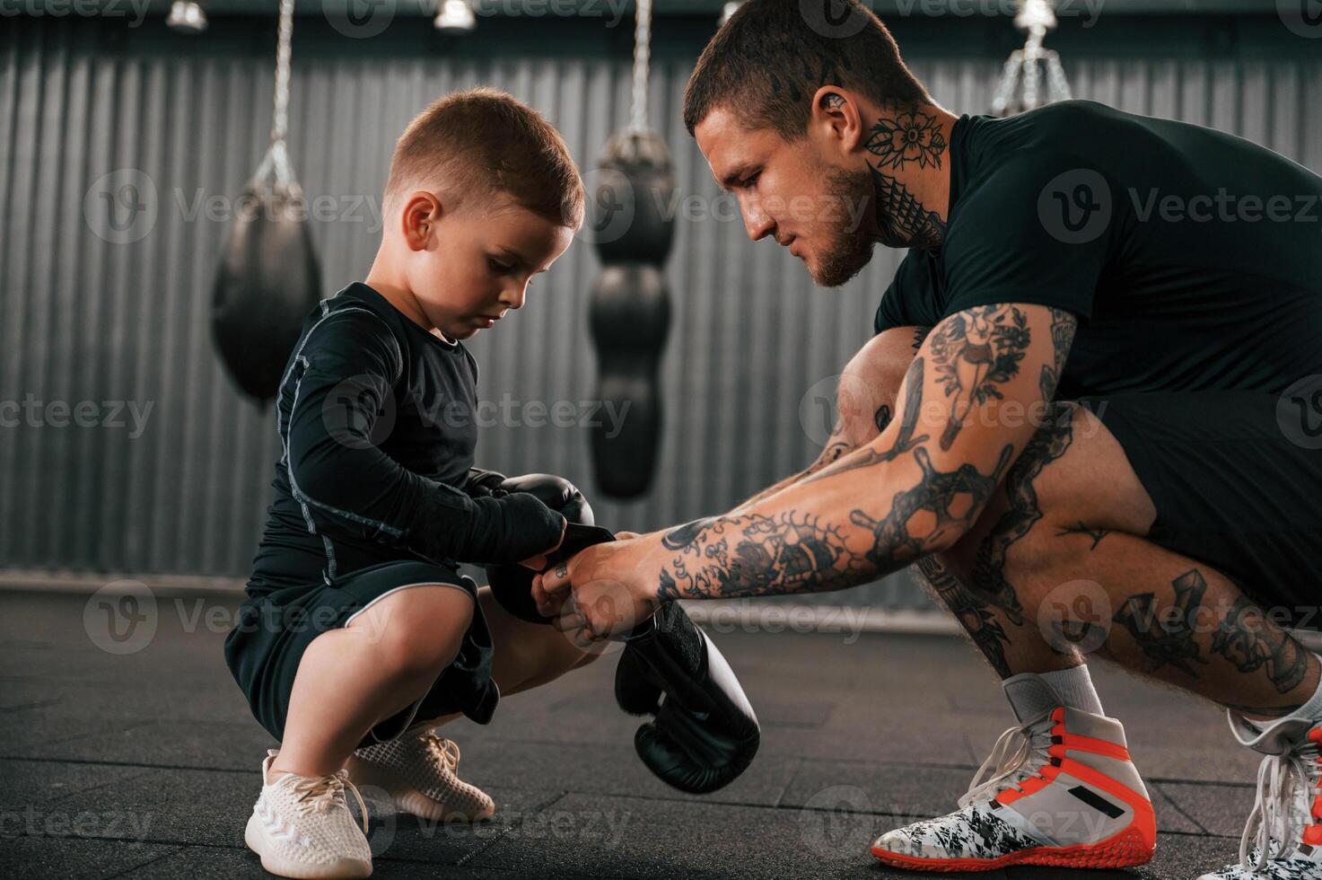 Man is helping kid with learning and practicing. Coach is teaching the boy box techniques indoors photo