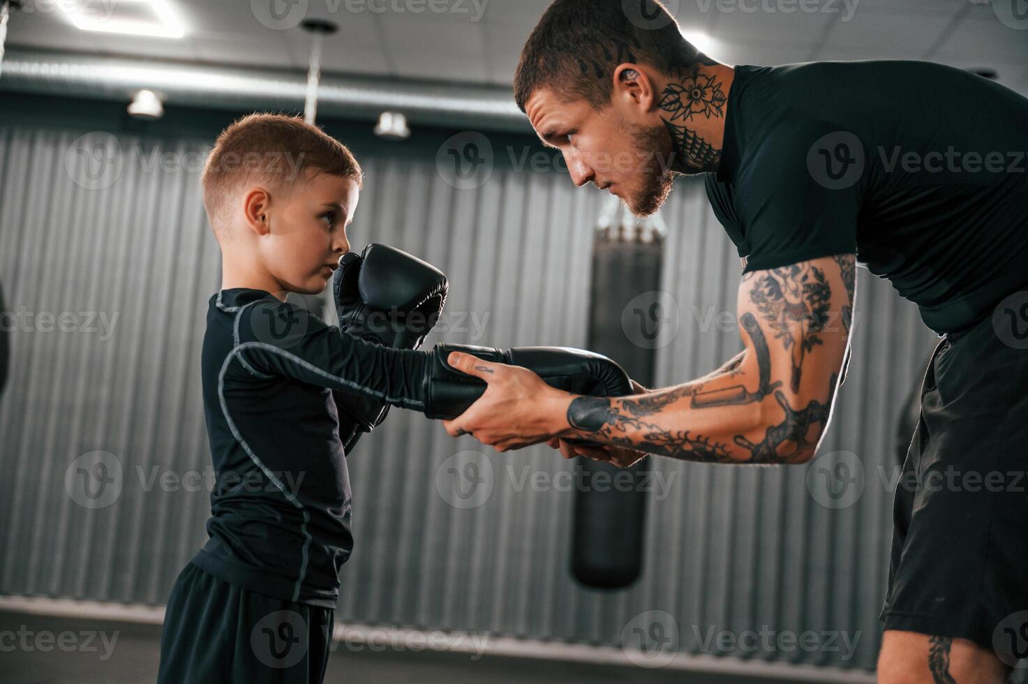 Man is helping child to wear the glowes. Coach is teaching the boy box techniques indoors photo