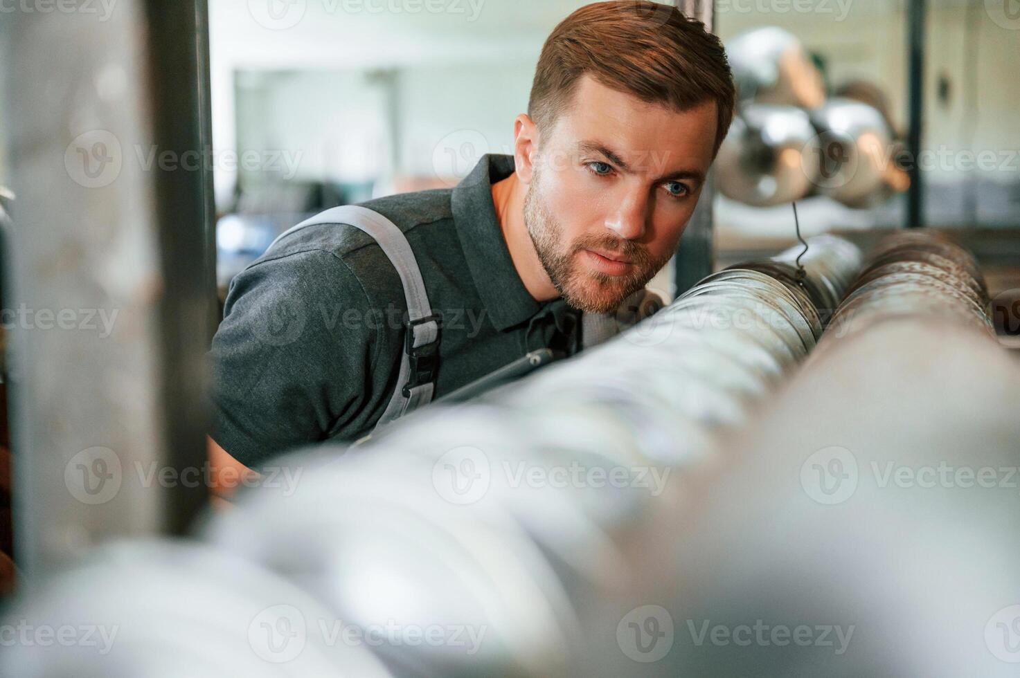 Measuring lenght of metal pieces. Man in uniform is in workstation developing details of agriculture technique,, photo