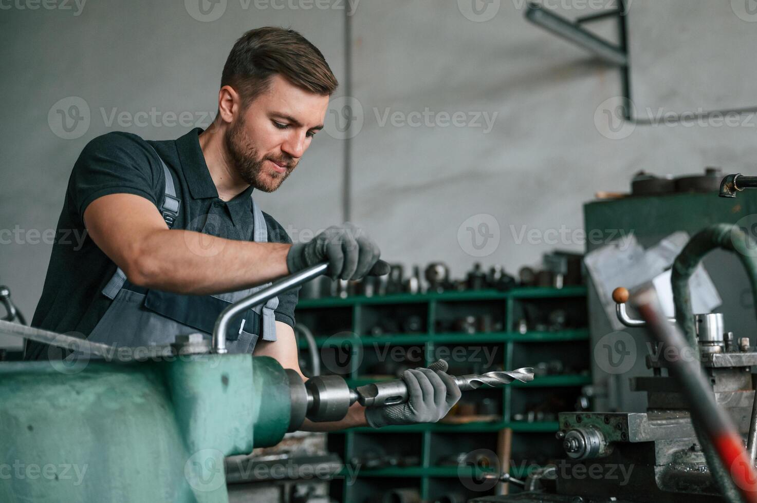 Working with metal. Man in uniform is indoors developing details of agriculture technique.. photo