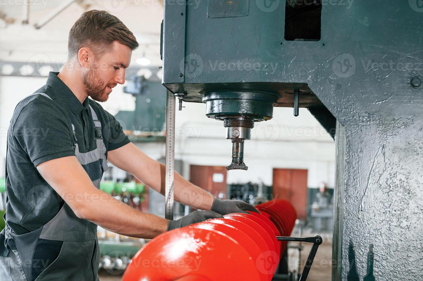 Measuring red colored sharp part. Man in uniform is in workstation developing details of agriculture technique.. photo