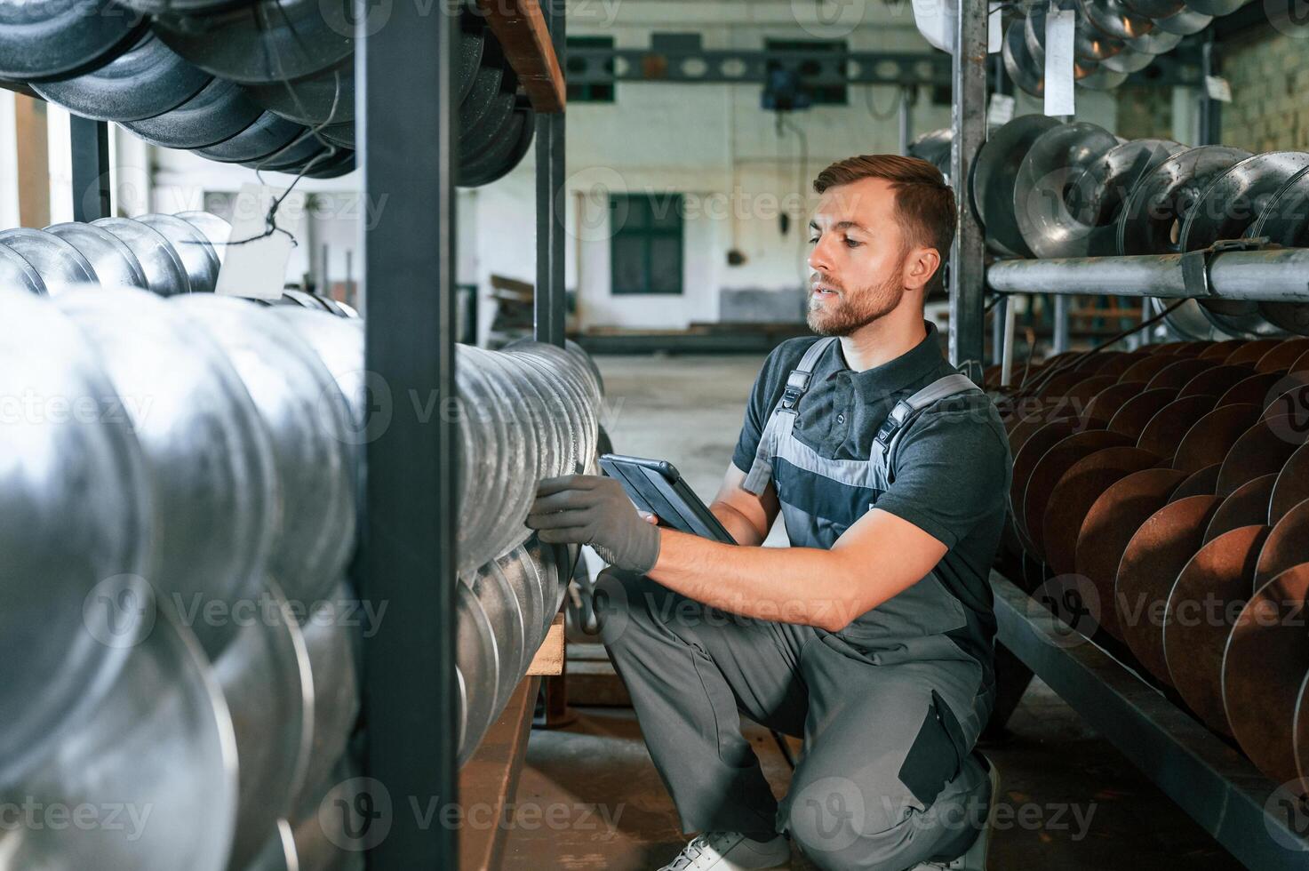 Checking number of parts. Man in uniform is in workstation developing details of agriculture technique. photo