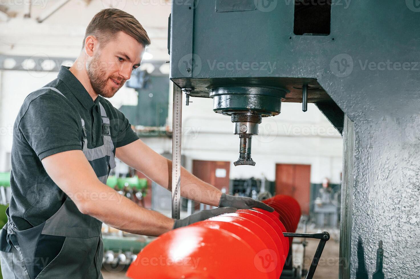 Measuring red colored sharp part. Man in uniform is in workstation developing details of agriculture technique.,. photo