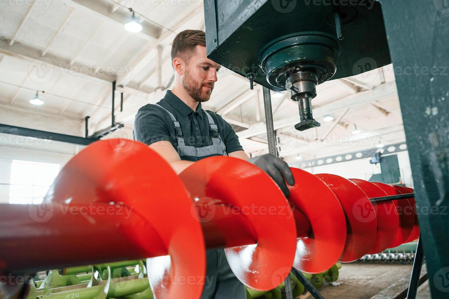 Measuring red colored sharp part. Man in uniform is in workstation developing details of agriculture technique. photo