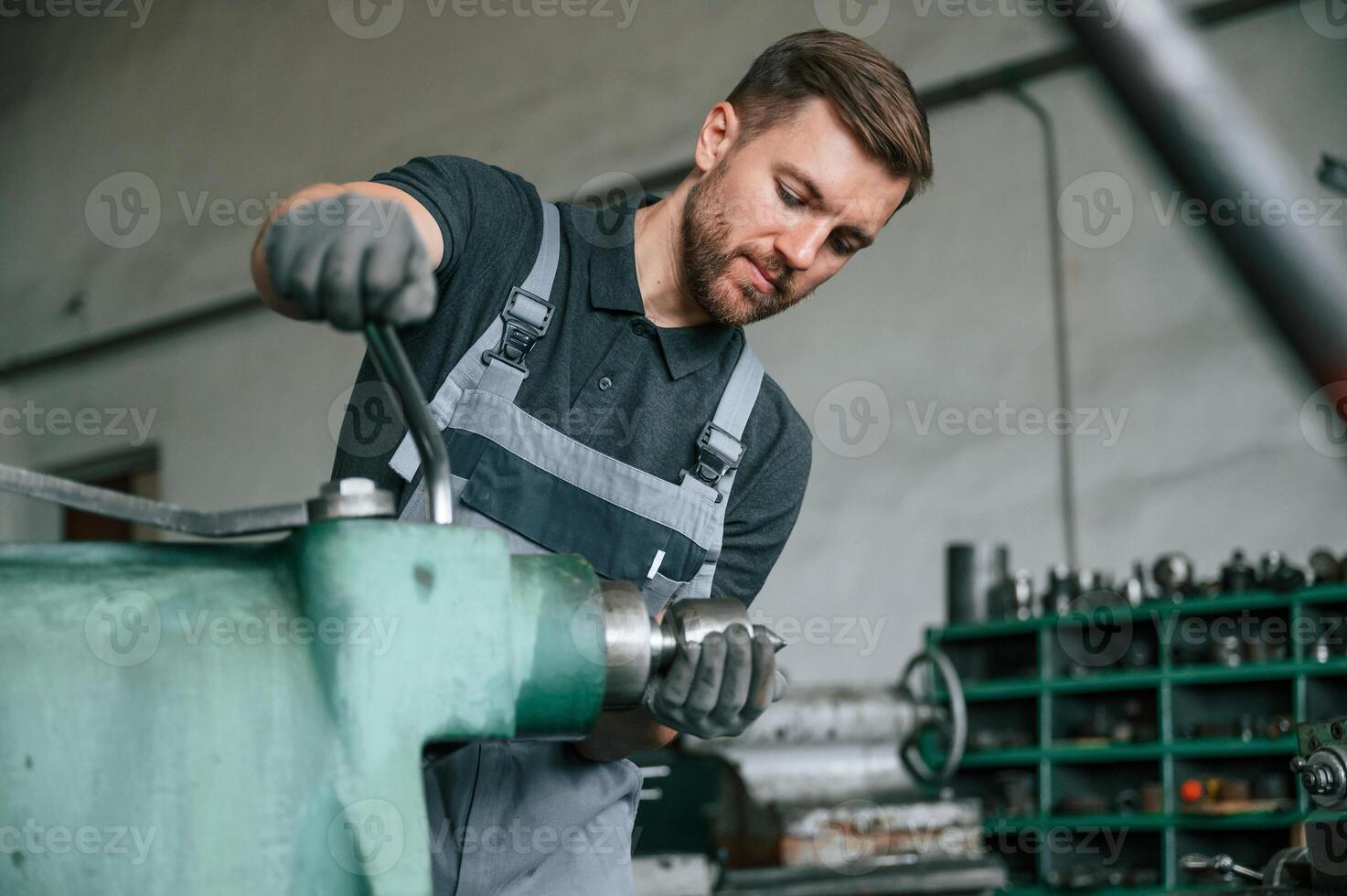 Working with metal... Man in uniform is indoors developing details of agriculture technique photo
