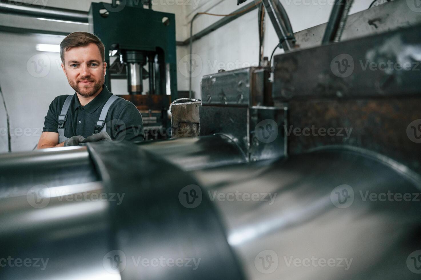 Holding part of metal construction. Man in uniform is in workstation developing details of agriculture technique photo