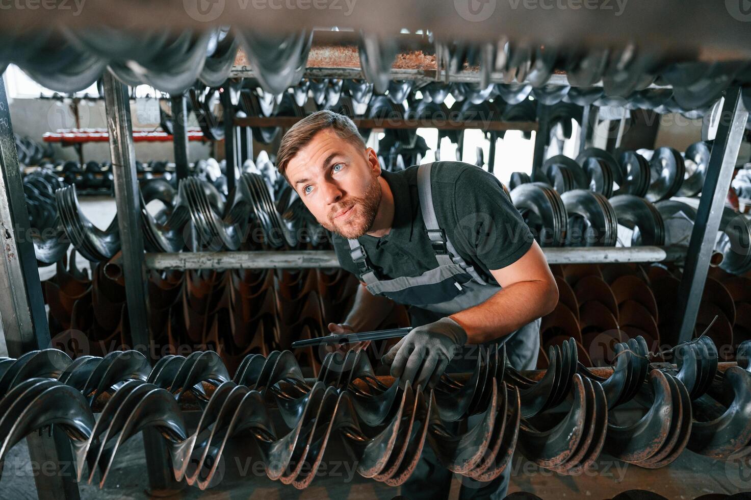 Checking number of parts. Man in uniform is in workstation developing details of agriculture technique., photo
