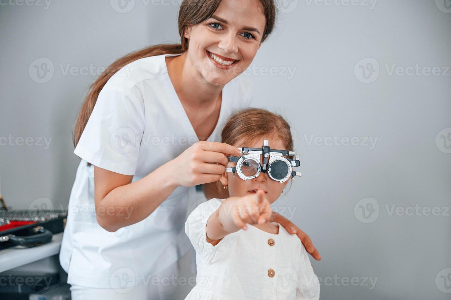 Looking forward, .correcting eye sight by device. Little girl have their vision checking in the clinic by help of the female doctor photo