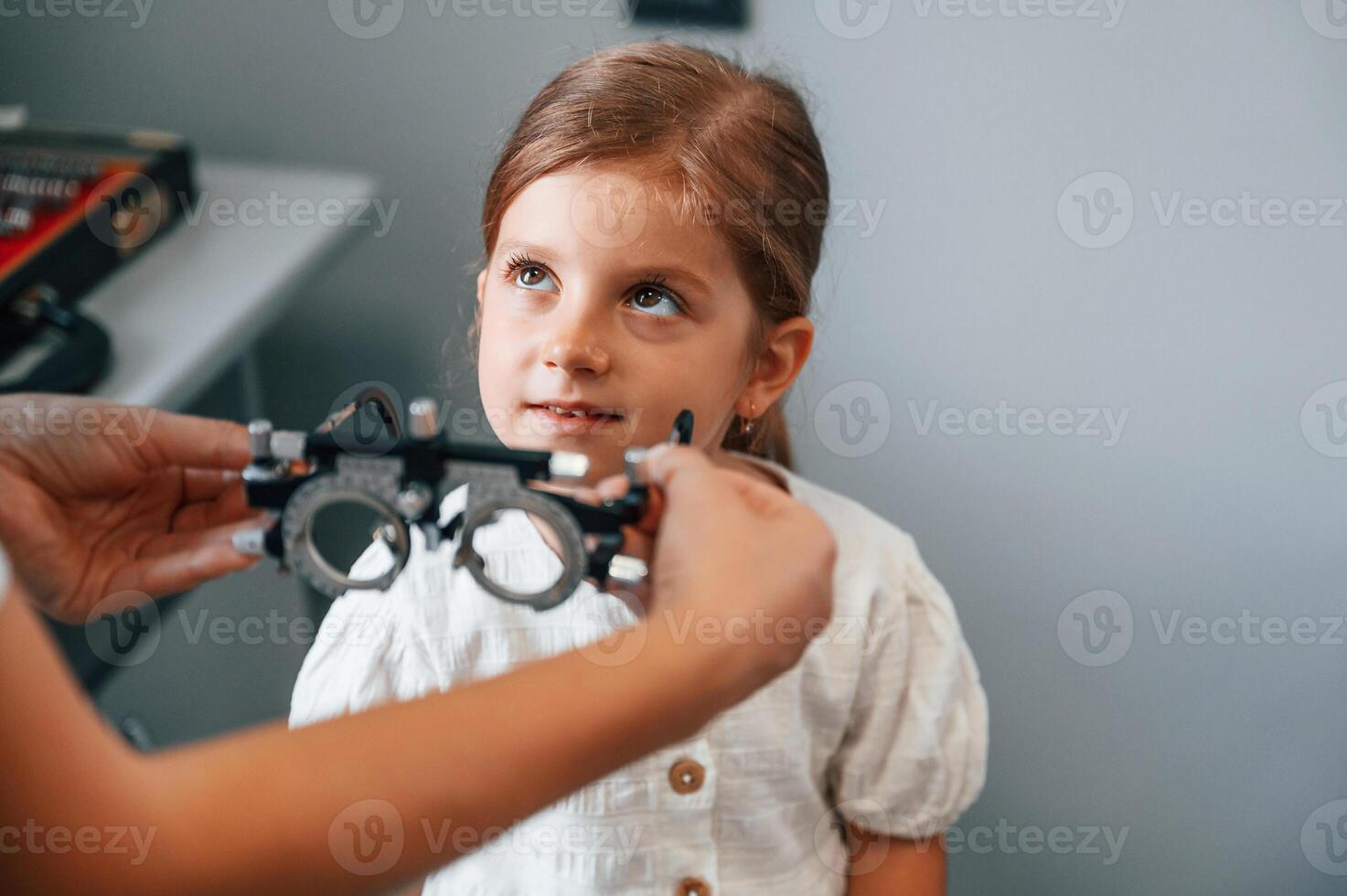 In special device with lenses.. Little girl have their vision checking in the clinic by help of the female doctor photo