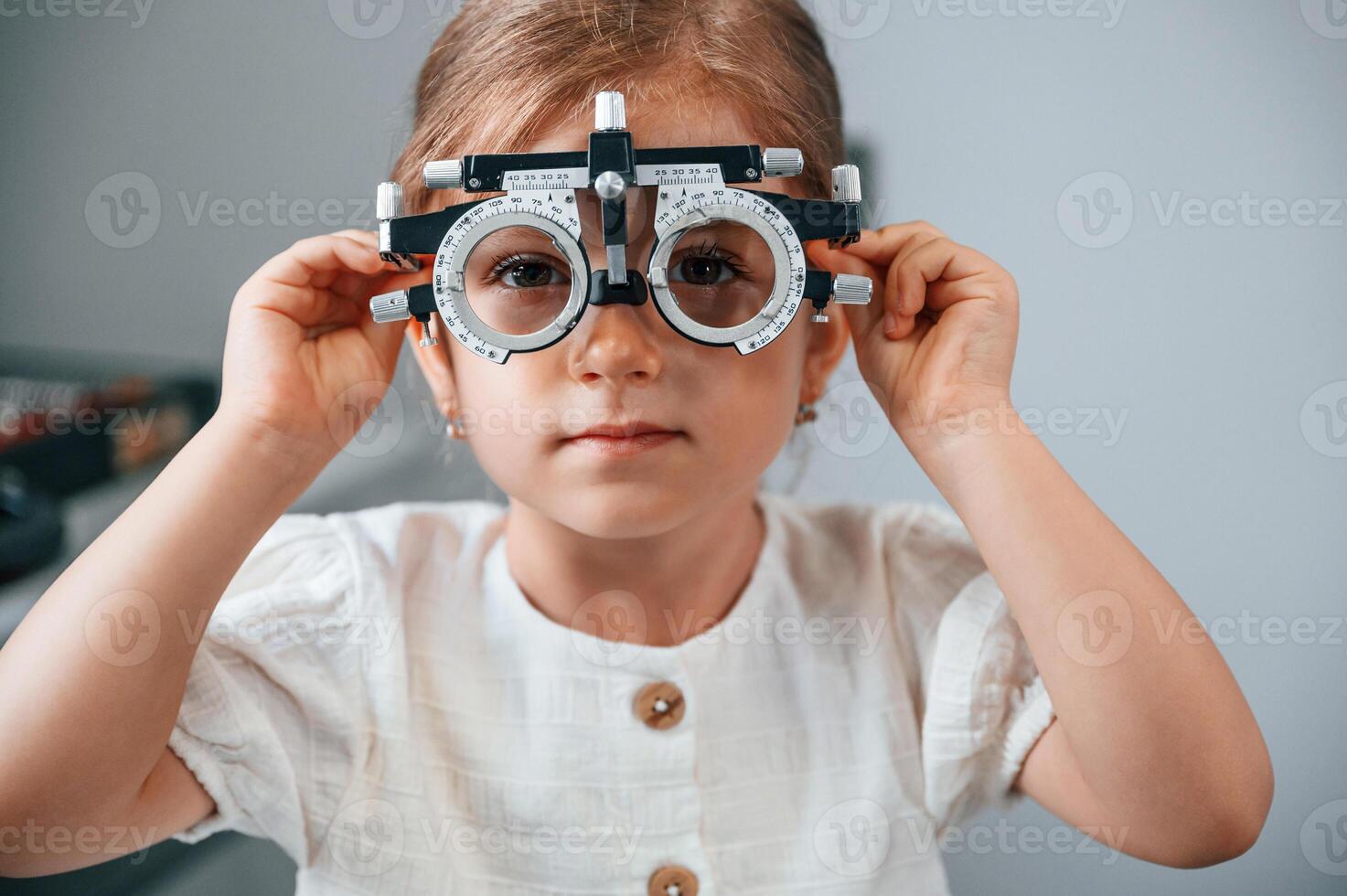In, special device with lenses.. Little girl have their vision checking in the clinic by help of the female doctor photo