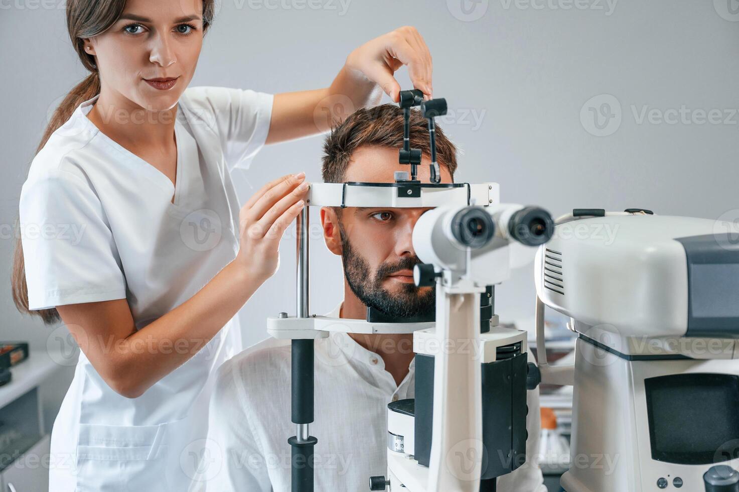 Man's vision checked by female doctor in the clinic by using special optometrist device photo