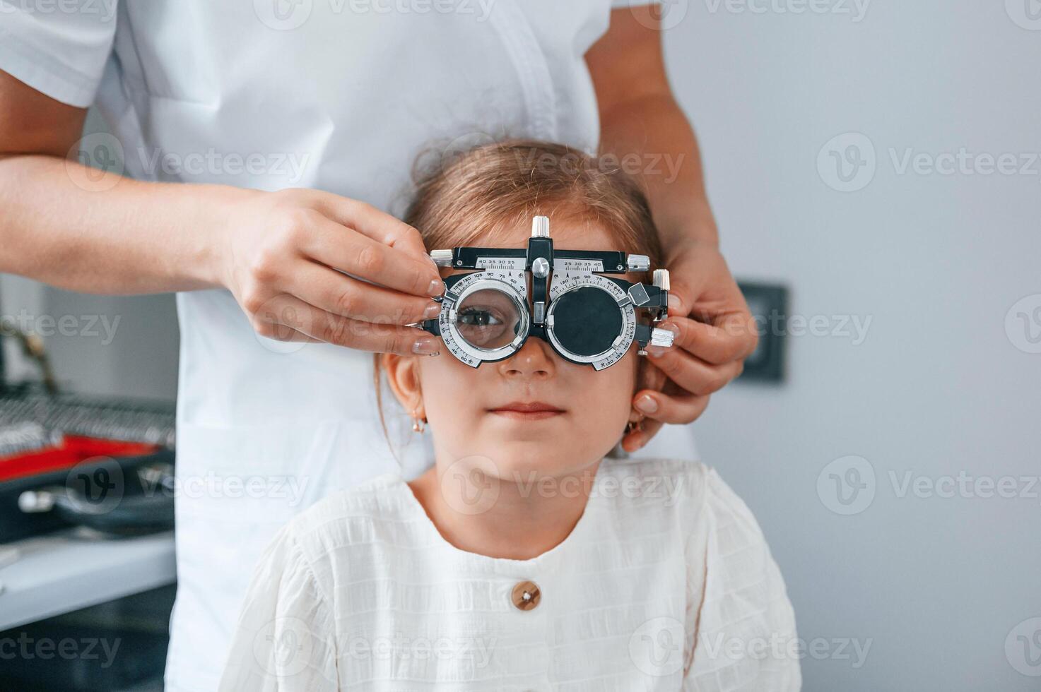 In special device with lenses. Little girl ,have their vision checking in the clinic by help of the female doctor photo