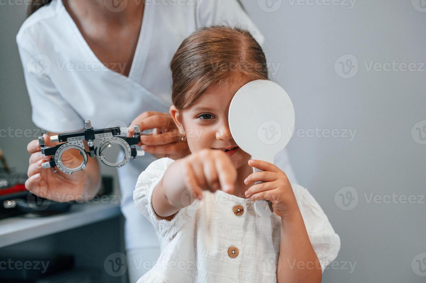 Covering left eye.. Little girl have their vision checking in the clinic by help of the female doctor photo