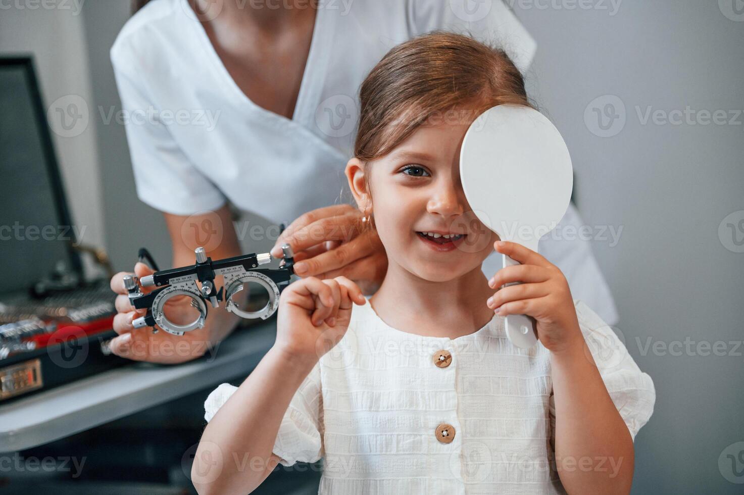 Covering left eye. Little girl have their vision checking in the clinic by help of the female doctor photo
