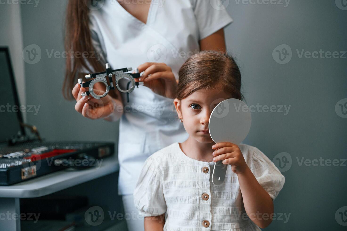 Covering left eye.. Little girl have, their vision checking in the clinic by help of the female doctor photo