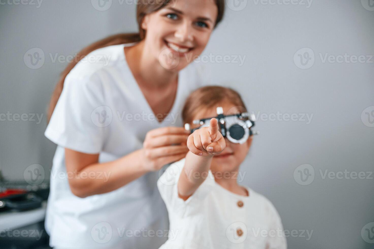 Looking forward,, correcting eye sight by device. Little girl have their vision checking in the clinic by help of the female doctor photo