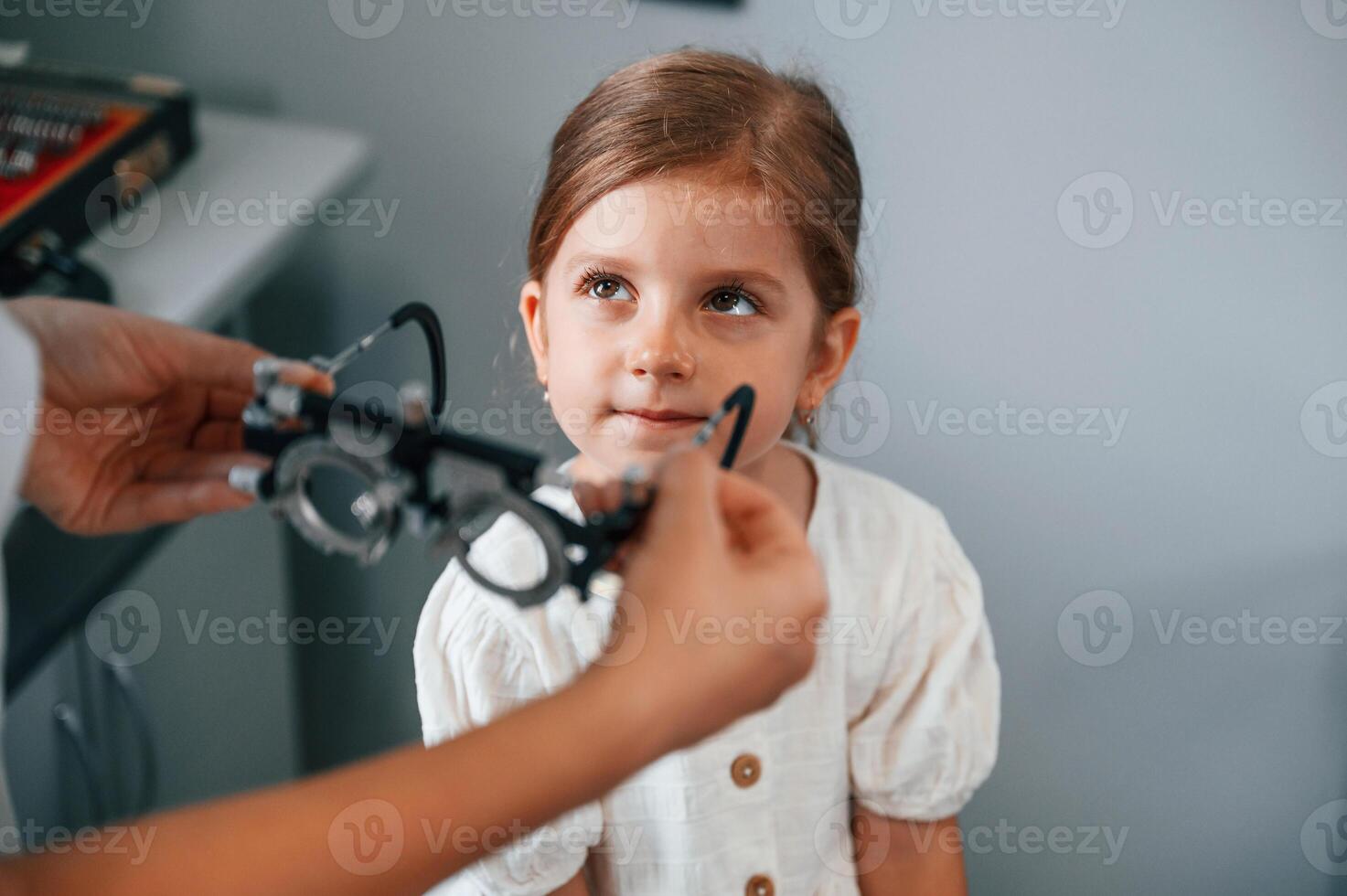 In special, device with lenses. Little girl have their vision checking in the clinic by help of the female doctor photo