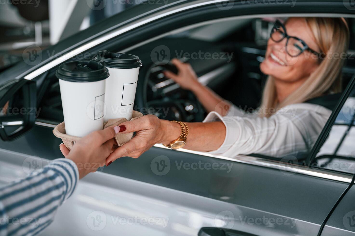 Taking cups of drinks.. Woman in white formal clothes is in the car dealership photo