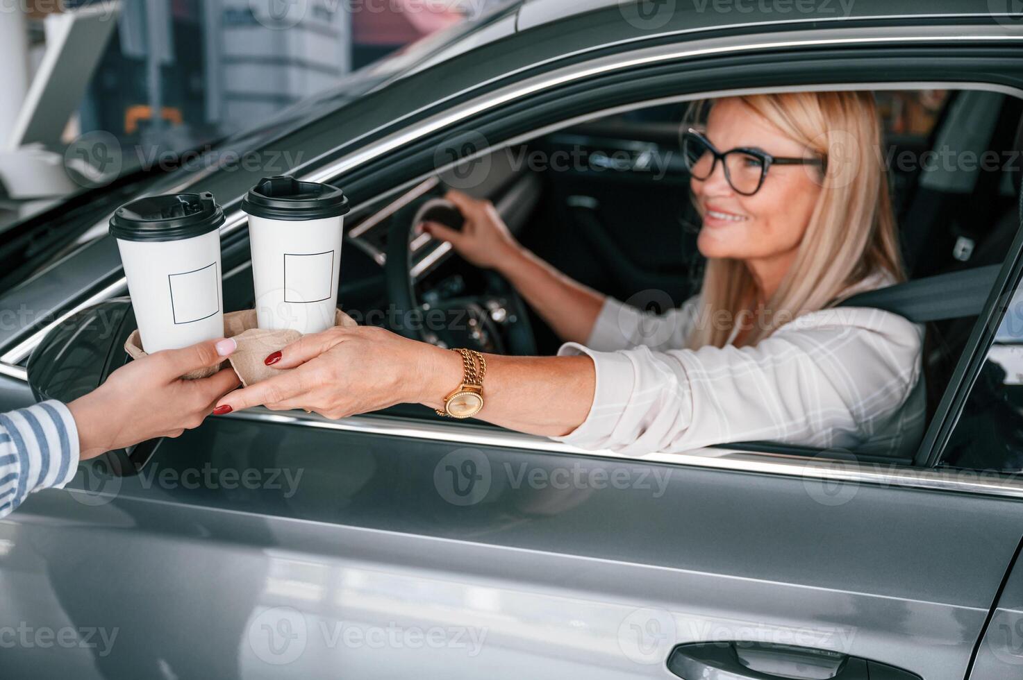 Taking cups of drinks., Woman in white formal clothes is in the car dealership photo
