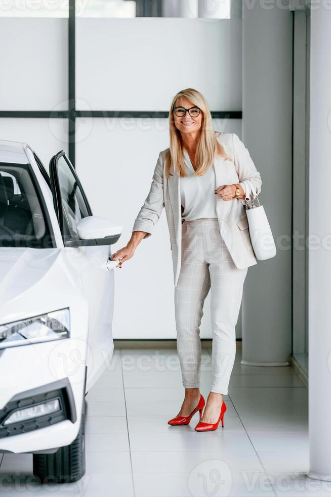 Going to the automobile. Woman in white formal clothes is in the car dealership photo