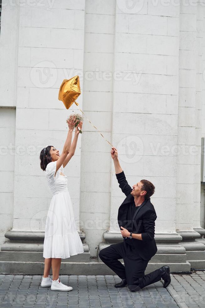 Playing with golden colored baloon. Beautiful bride with his fiance is celebrating wedding outdoors. photo