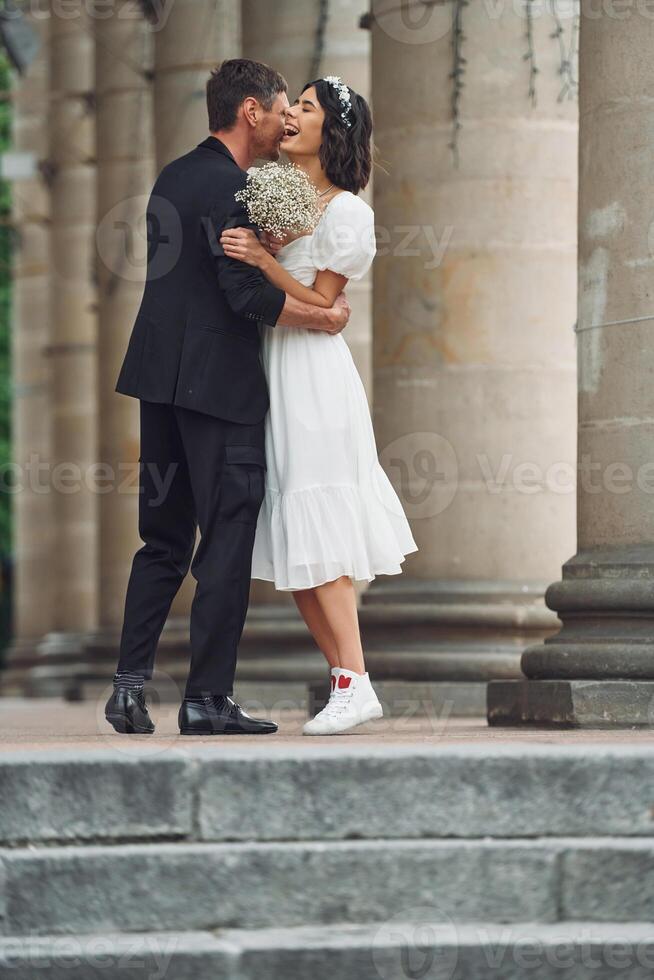 Standing and posing near building. ,Beautiful bride with his fiance is celebrating wedding outdoors photo
