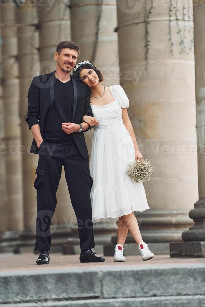 Standing and posing near building. ,.Beautiful bride with his fiance is celebrating wedding outdoors photo