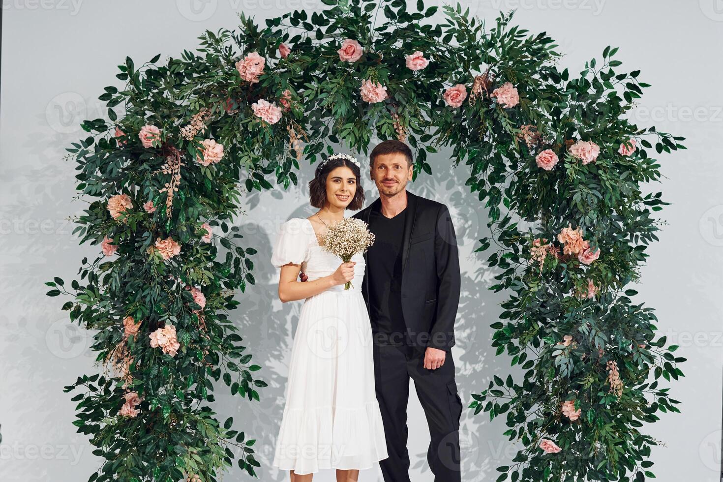 Standing against flowers. .Beautiful bride with his fiance is on the wedding photo