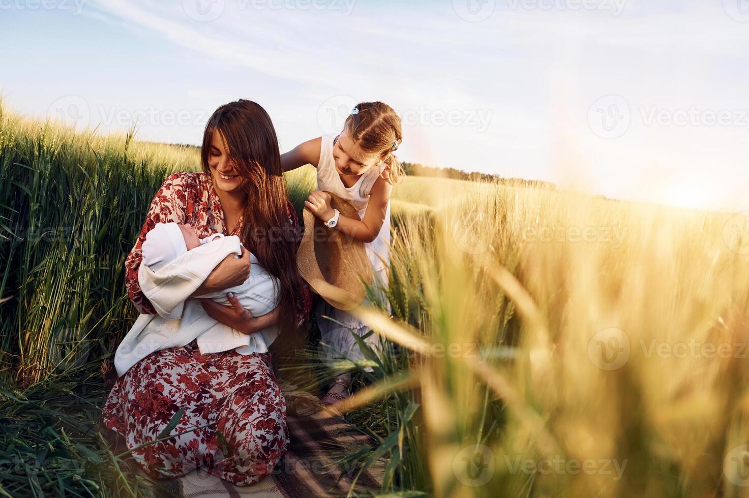 Looking at the newborn baby. ,Mother with girl is on the field at sunny day together photo