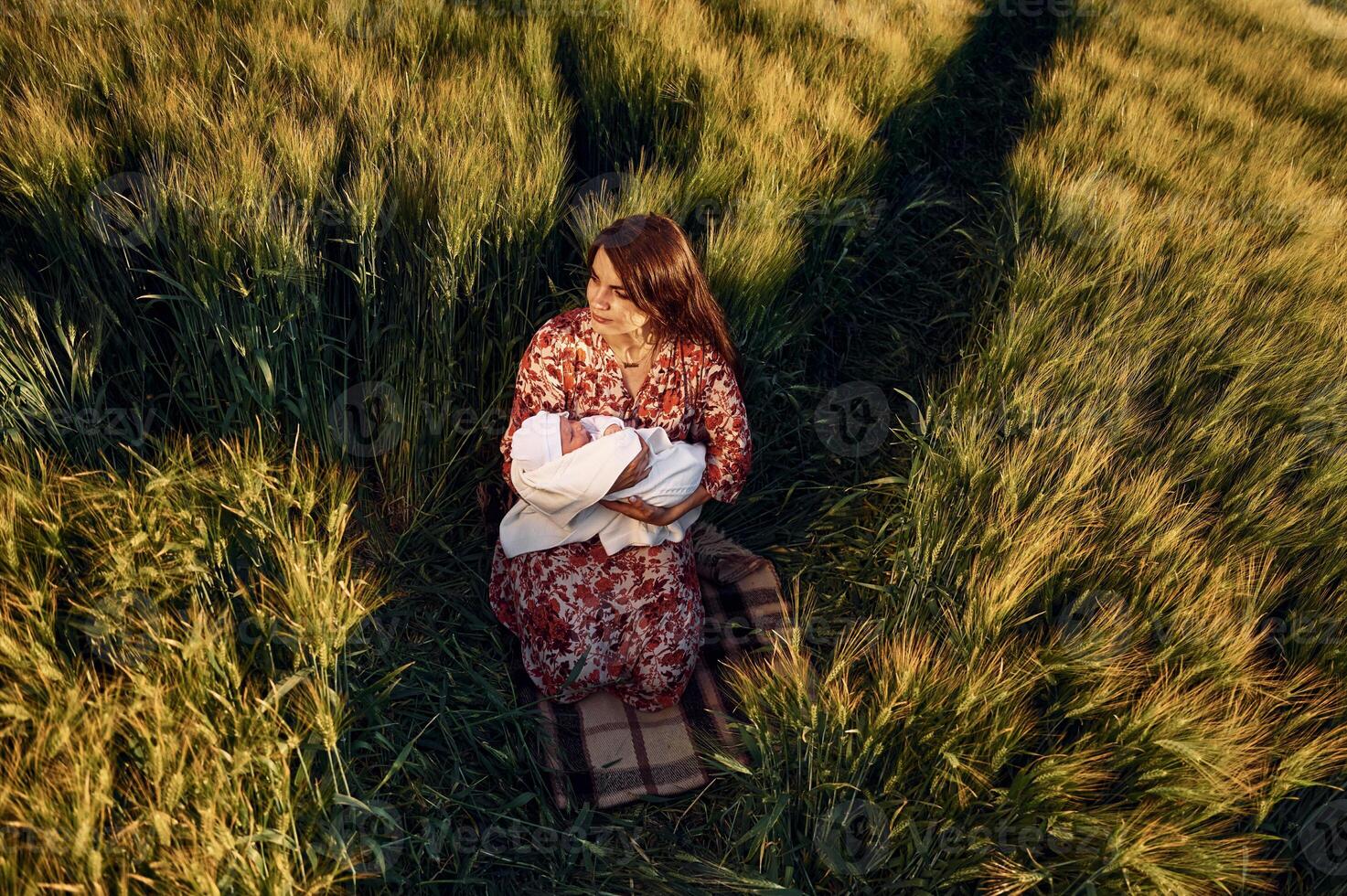 Sitting on the ground. Gorgeous woman is on the agricultural field with her newborn baby photo