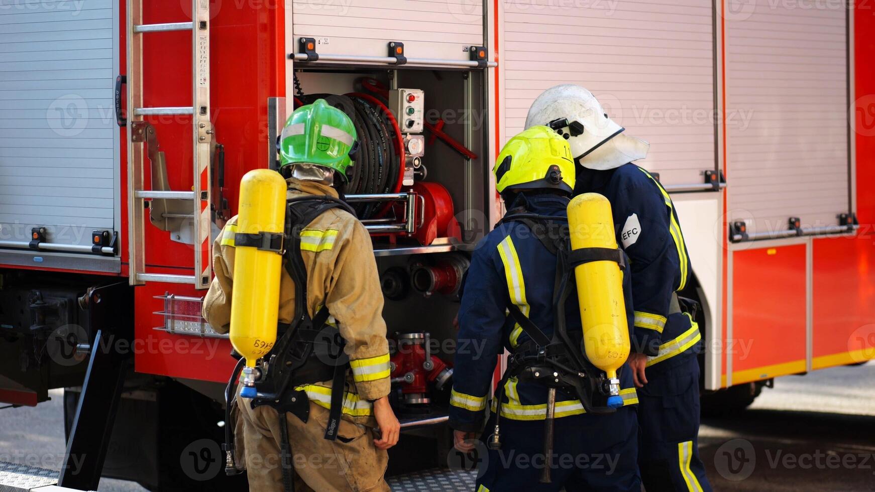 Young firemen prepare to extinguishing fire near big truck. Male firefighters in full equipment ready to putting out fire near a red car. Concept of saving lives and heroic profession. Slow motion photo