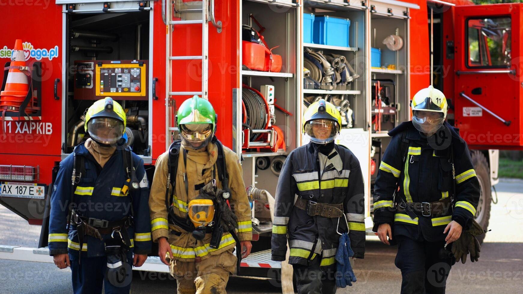 Portrait of male and female firefighters in helmets and protective uniforms standing near big red car. Young confident fireman and firewoman in full equipment posing against background of fire engine photo