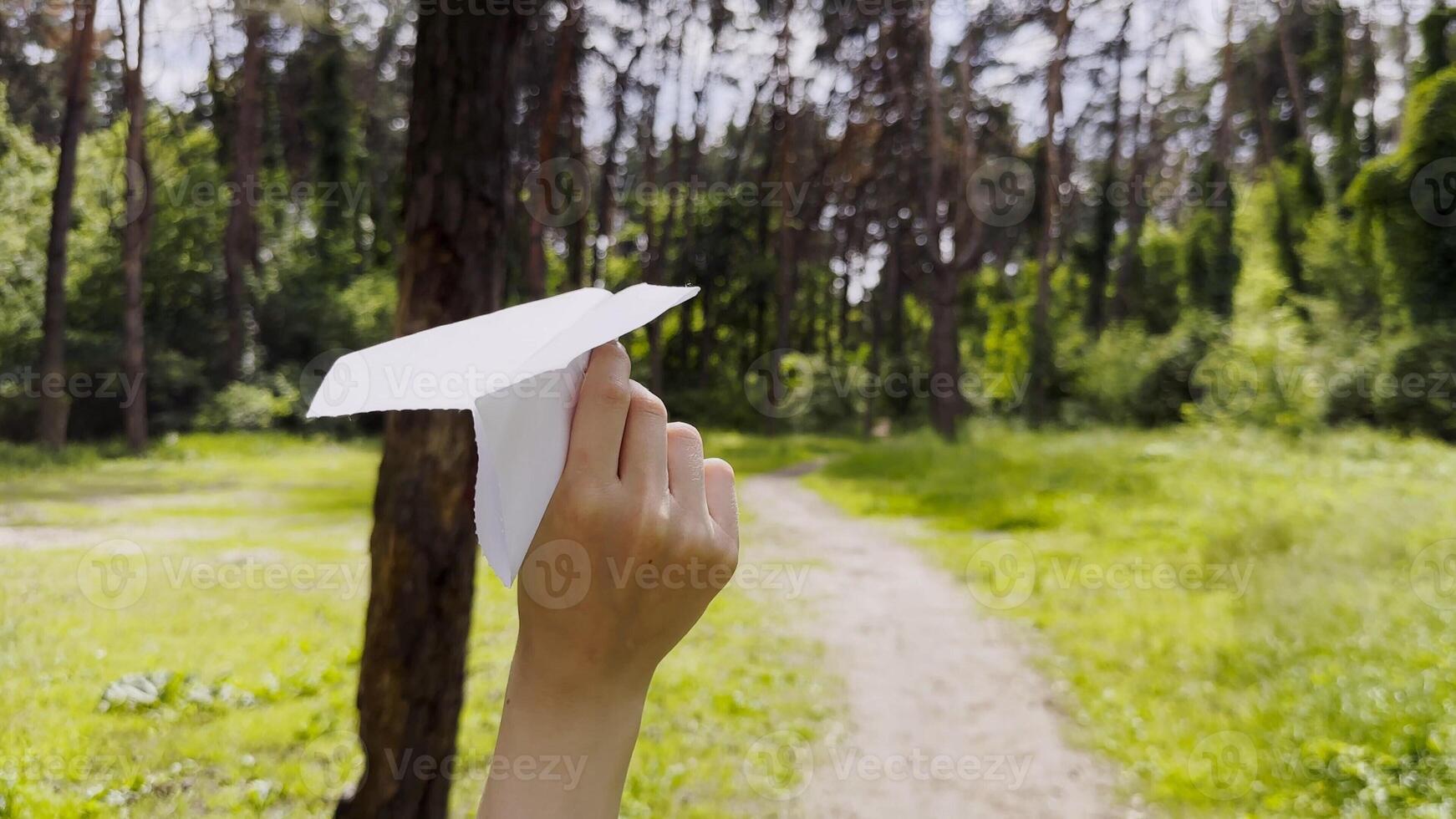 Female hand playing with paper airplane at summer forest. Girl walking with toy plane at woodland on sunny day. Young woman having fun at nature. Concept of leisure outdoor. Close up photo