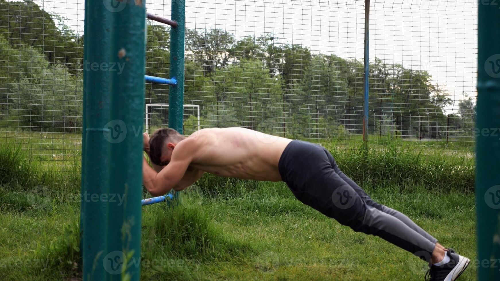 Young muscular athlete doing exercise on triceps at sport equipment outdoor. Male shirtless athlete working out at sport ground. Strong sporty man training at nature. Concept of healthy lifestyle photo