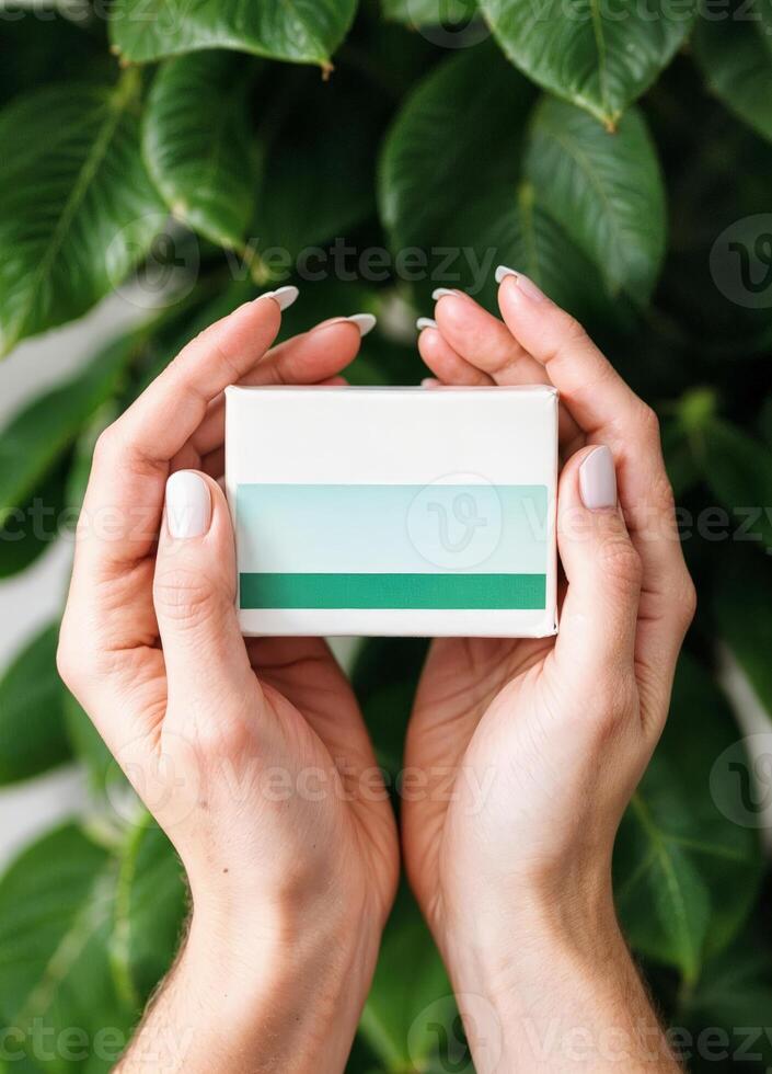 Hands holding a white soap bar box with green leaves on the background. Natural Herbal Product Box photo