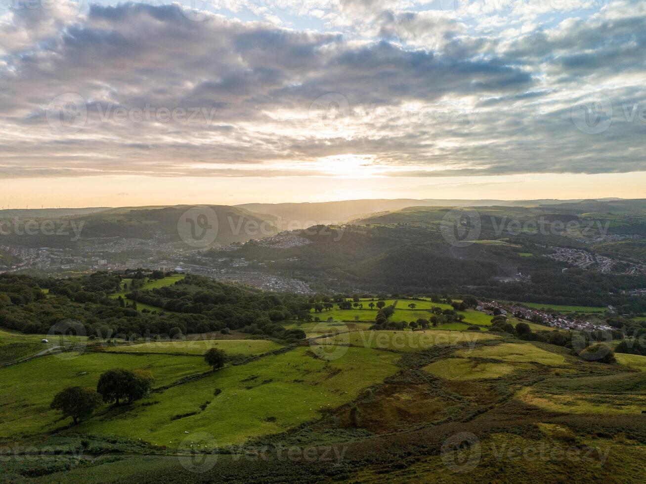Sun shining over green valley with towns in wales photo