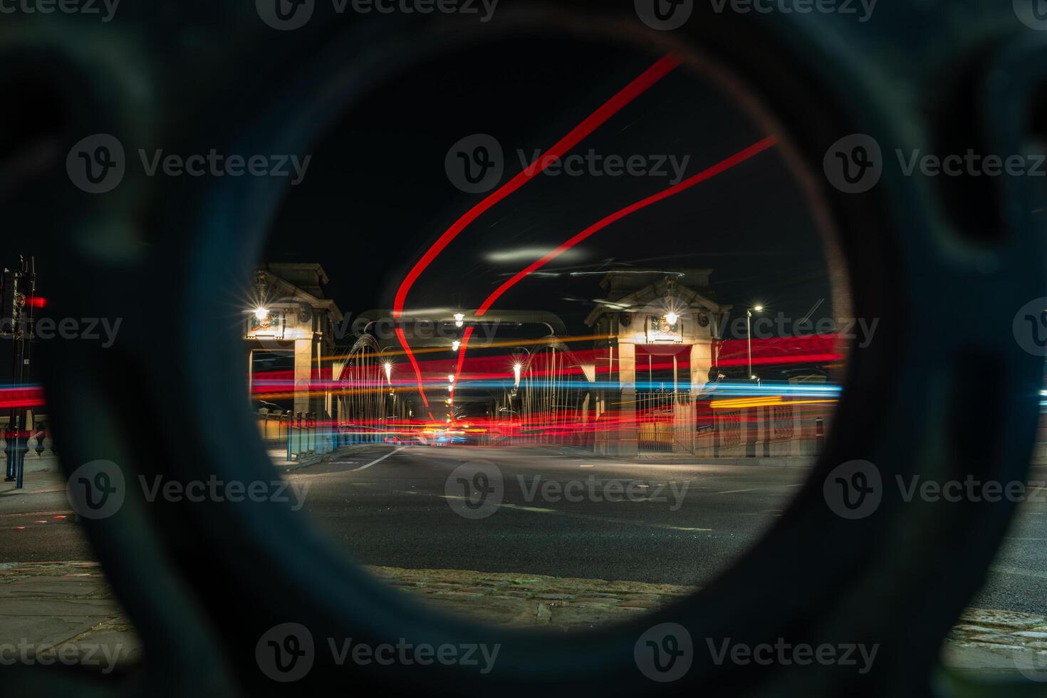 Light trails of cars driving over bridge at night seen through circular hole photo