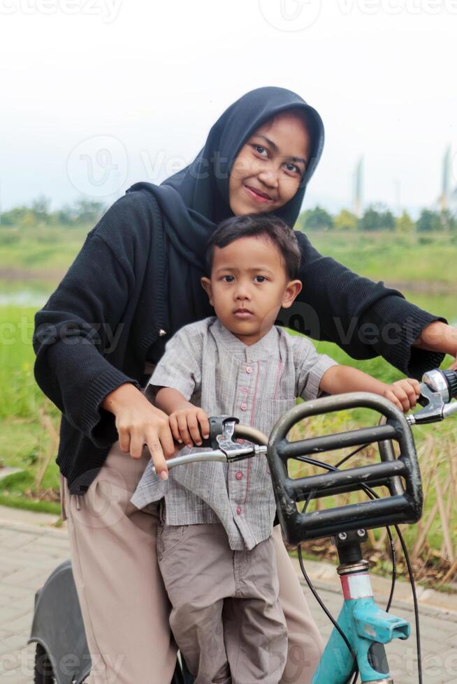 Muslim Sister and Little Brother Riding Bicycle Together in Park photo