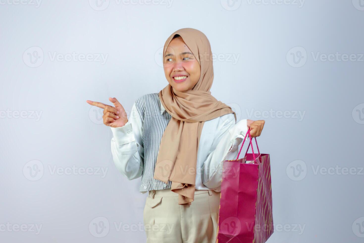 Cheerful Muslim Woman Holding Shopping Bag and Pointing Side photo