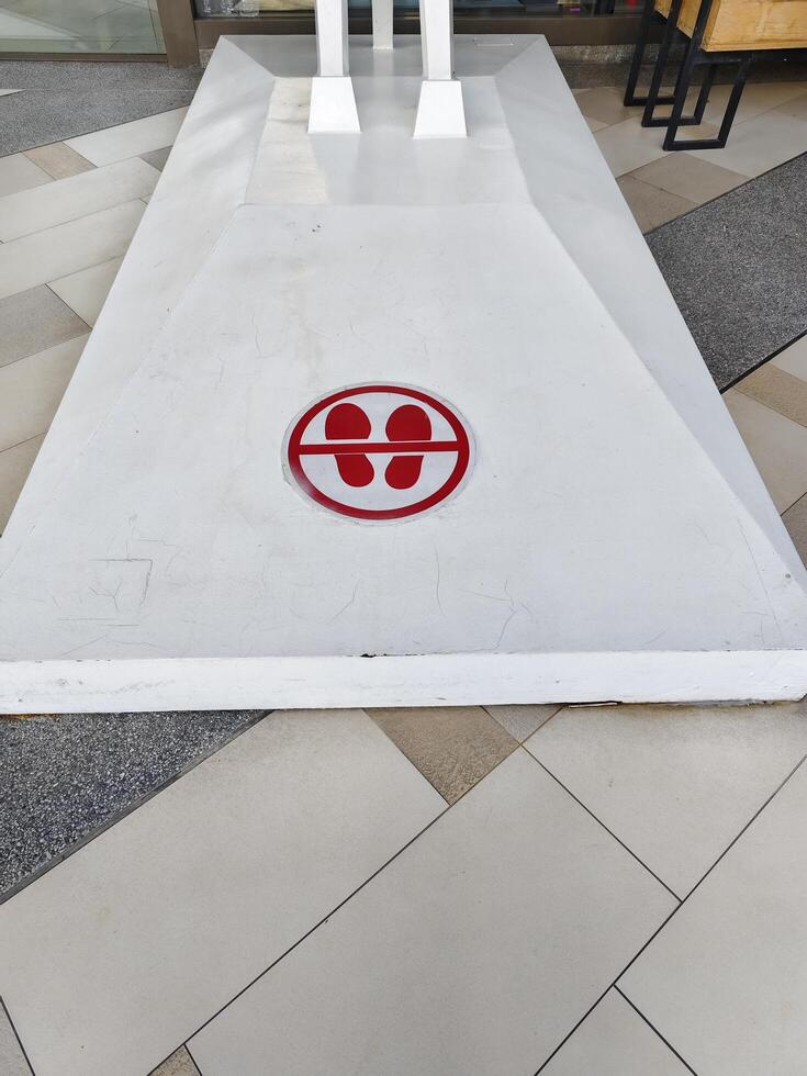 Do not put foot with shoe on white plate red sign in round shape. photo
