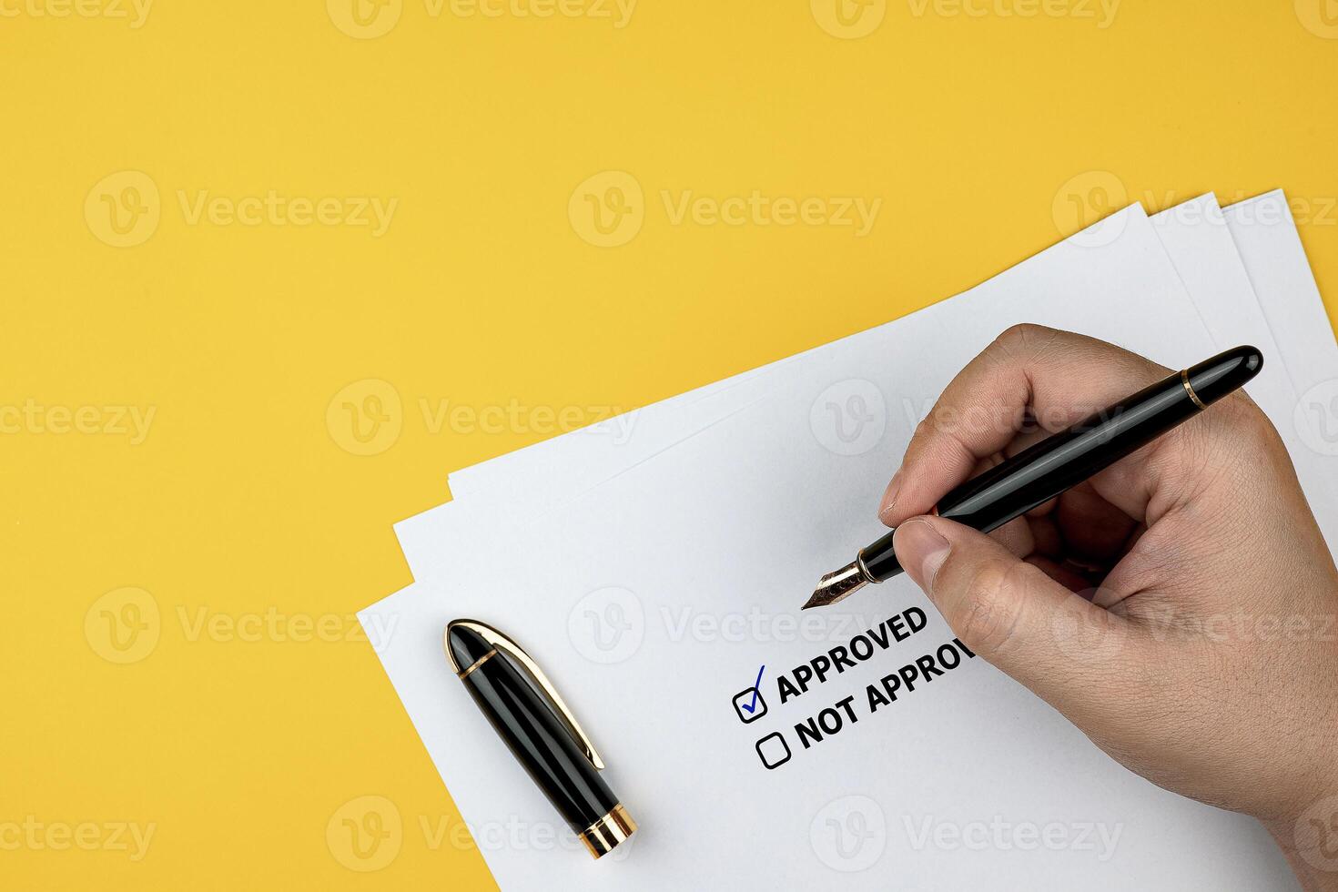Close-up view of hand holding checkered pen in square to approve document on yellow background. Concepts of organizational management, approval of operations, and budgets photo