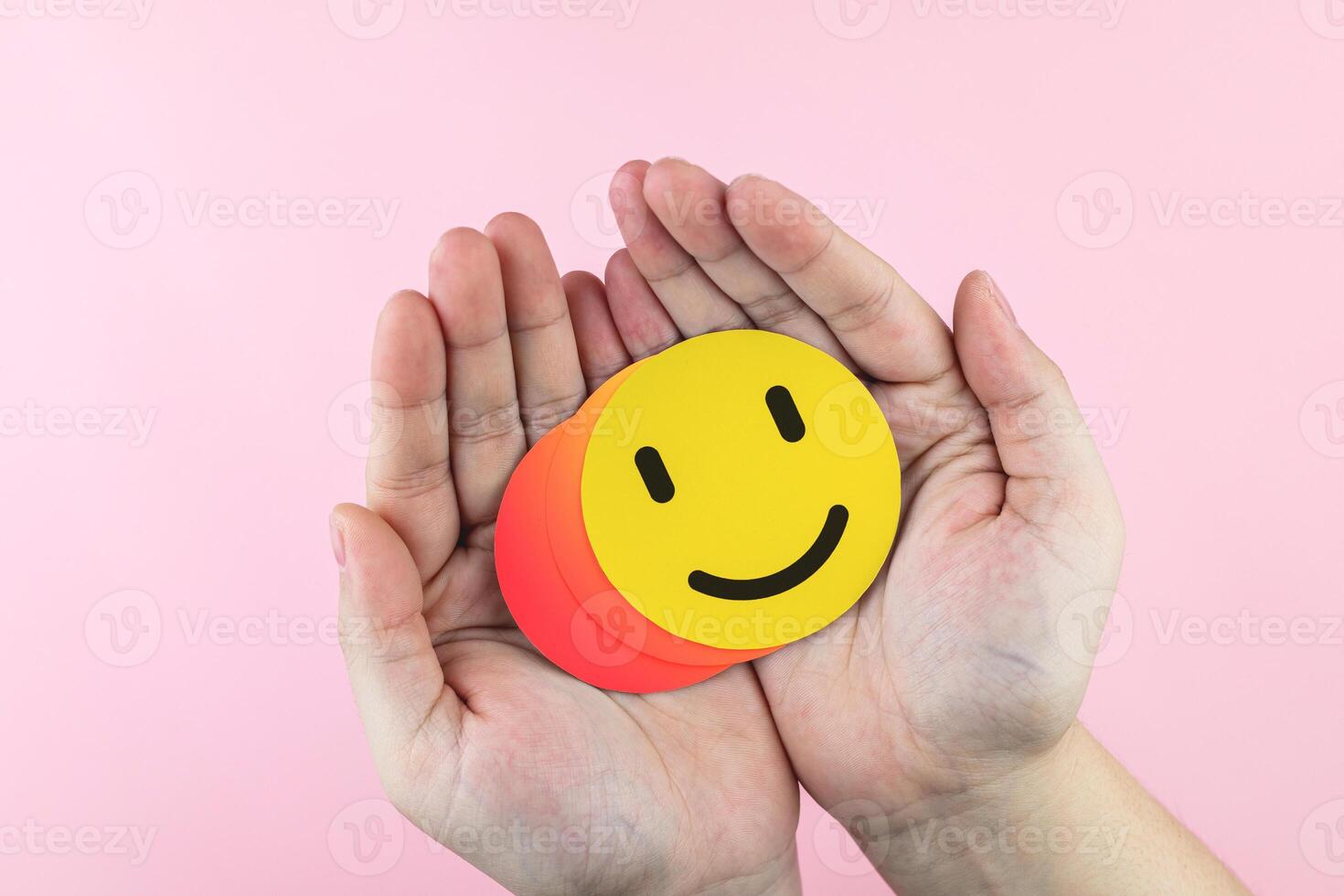 Hand holding paper circles with face happy emotions on pink background. Concept of business service, health assessment, excellent level measurement, and rating from customers photo