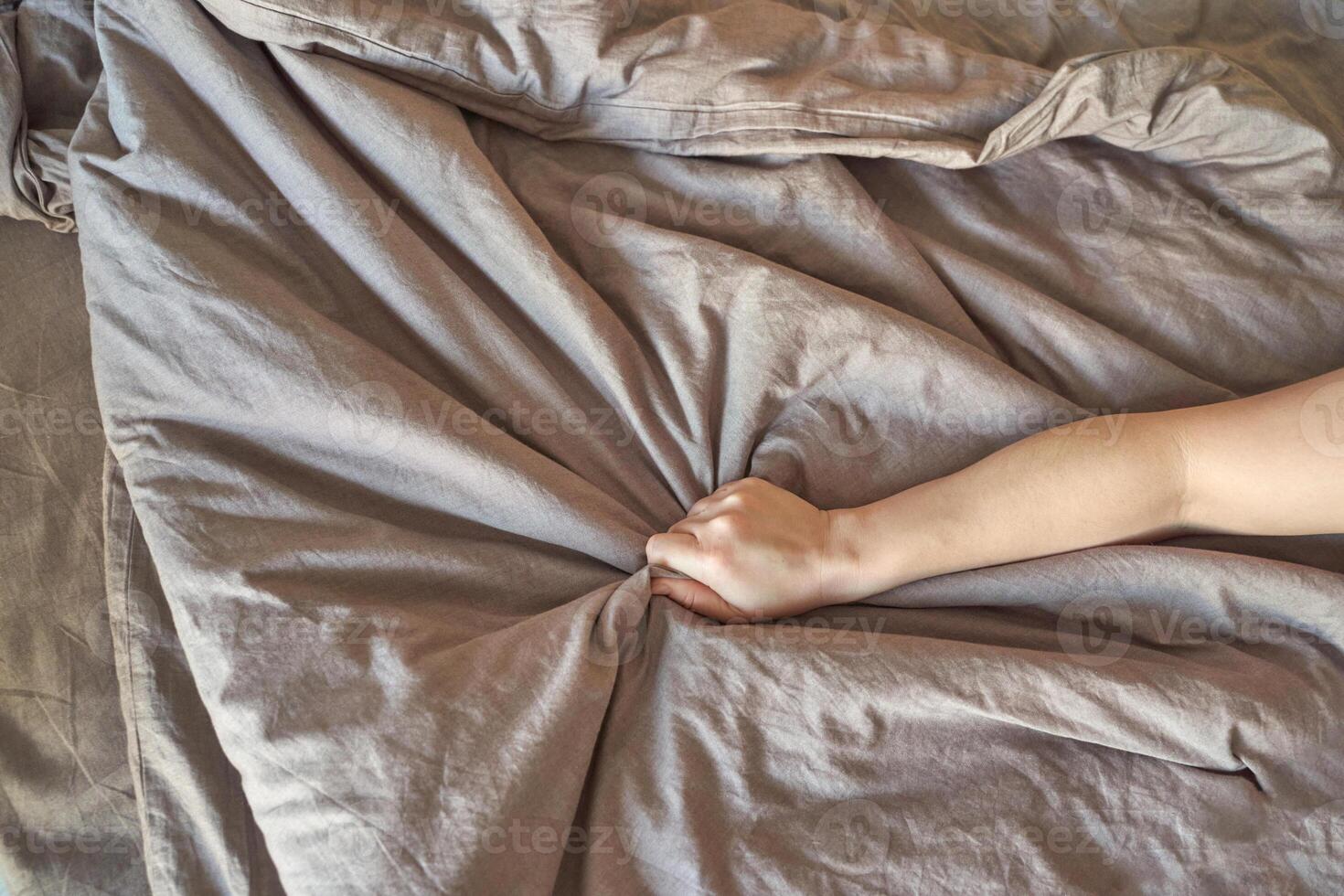 Close up of hand gripping beige bedsheet showing crumpled fabric texture and natural light. photo