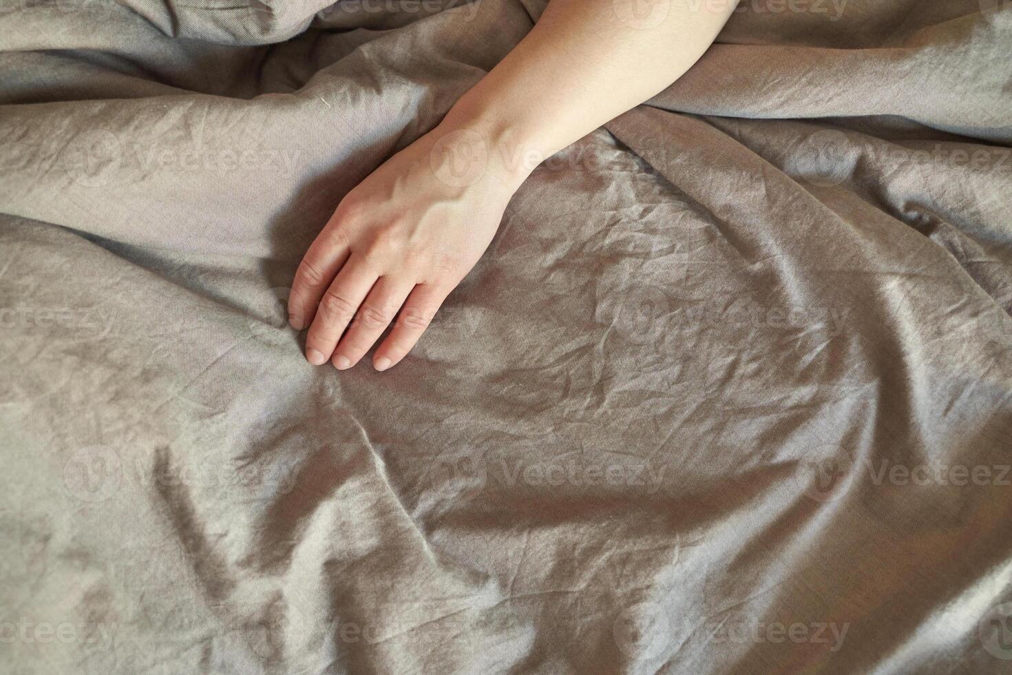 Female caucasian adult hand resting on wrinkled grey bedsheet in tranquil setting. photo