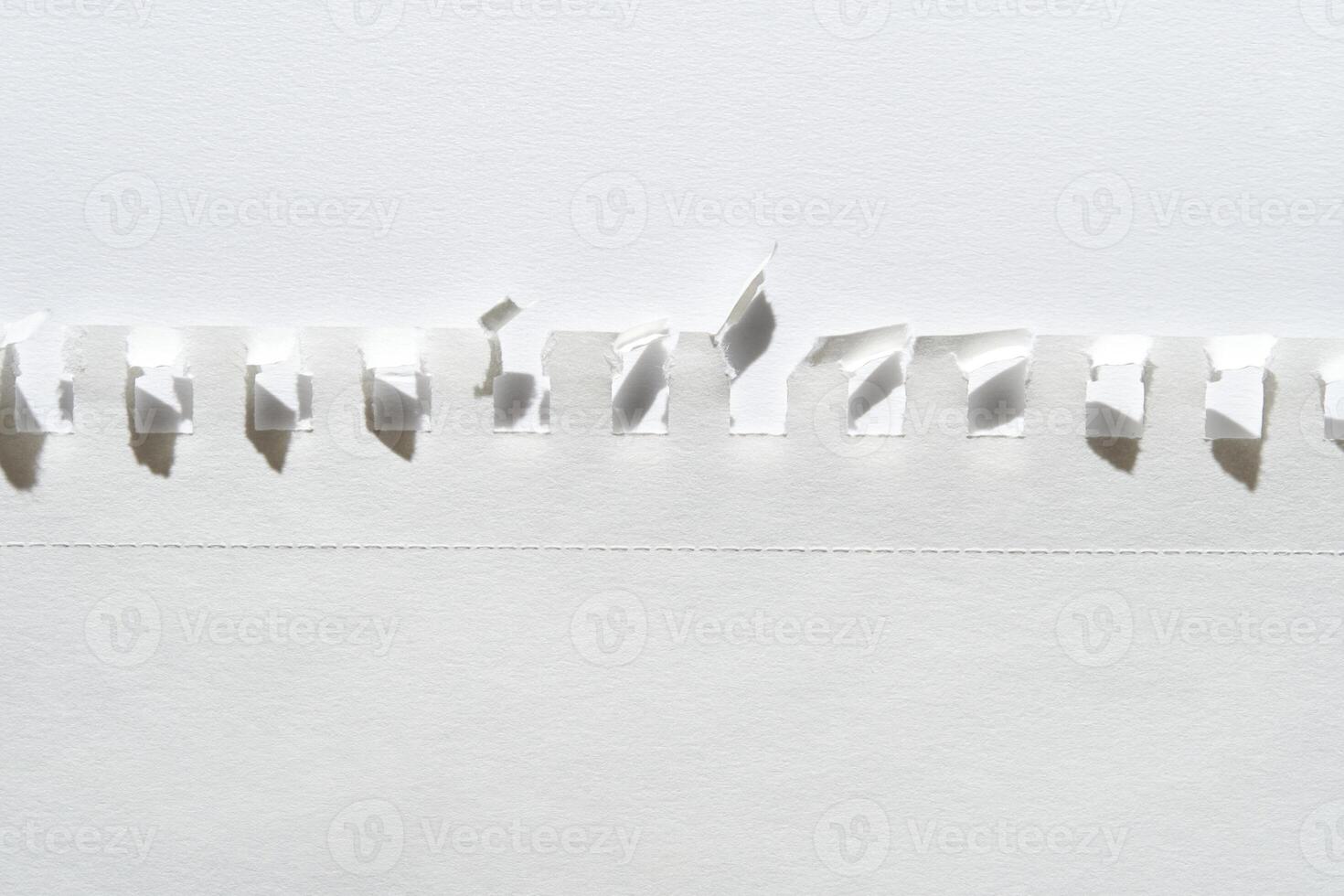 Close-up of torn white paper with perforated edge and folded tabs against light background. photo