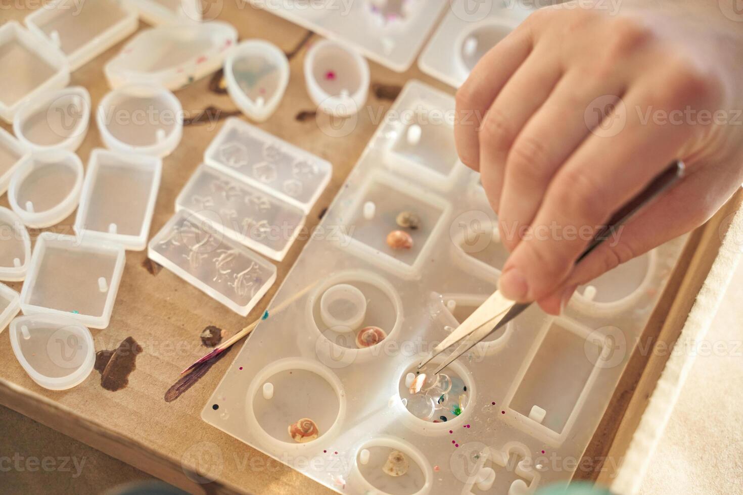 Close up of hand working with resin molds and small objects for jewelry crafting project. photo