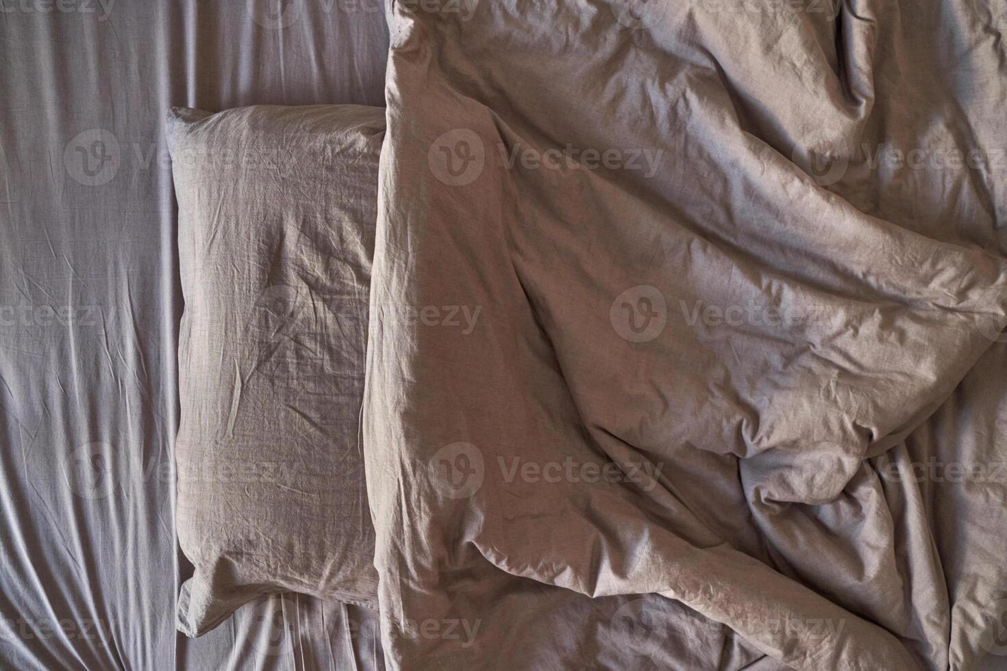 Empty unmade bed with wrinkled sheets and pillow in neutral tones depicting relaxation and home comfort. photo