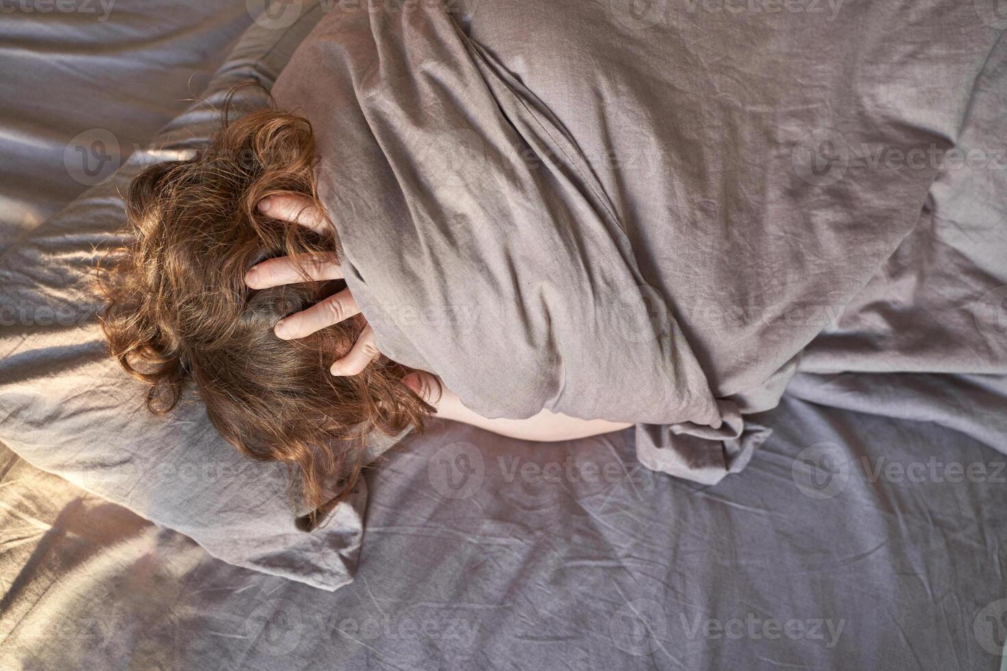 Female caucasian adult wrapped in grey blanket lying in bed with hands on head in relaxed morning mood. photo