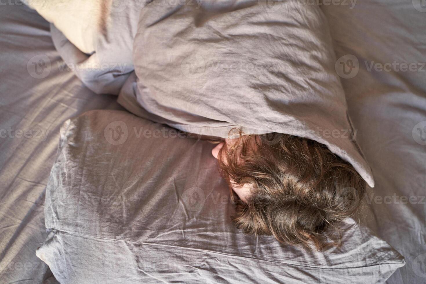 Young caucasian male sleeping under grey blanket with head on pillow, cozy restful scene in bedroom. photo